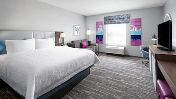 Una habitación de hotel con una cama grande, un escritorio con computadora, una silla, una ventana con cortinas y obras de arte en las paredes.