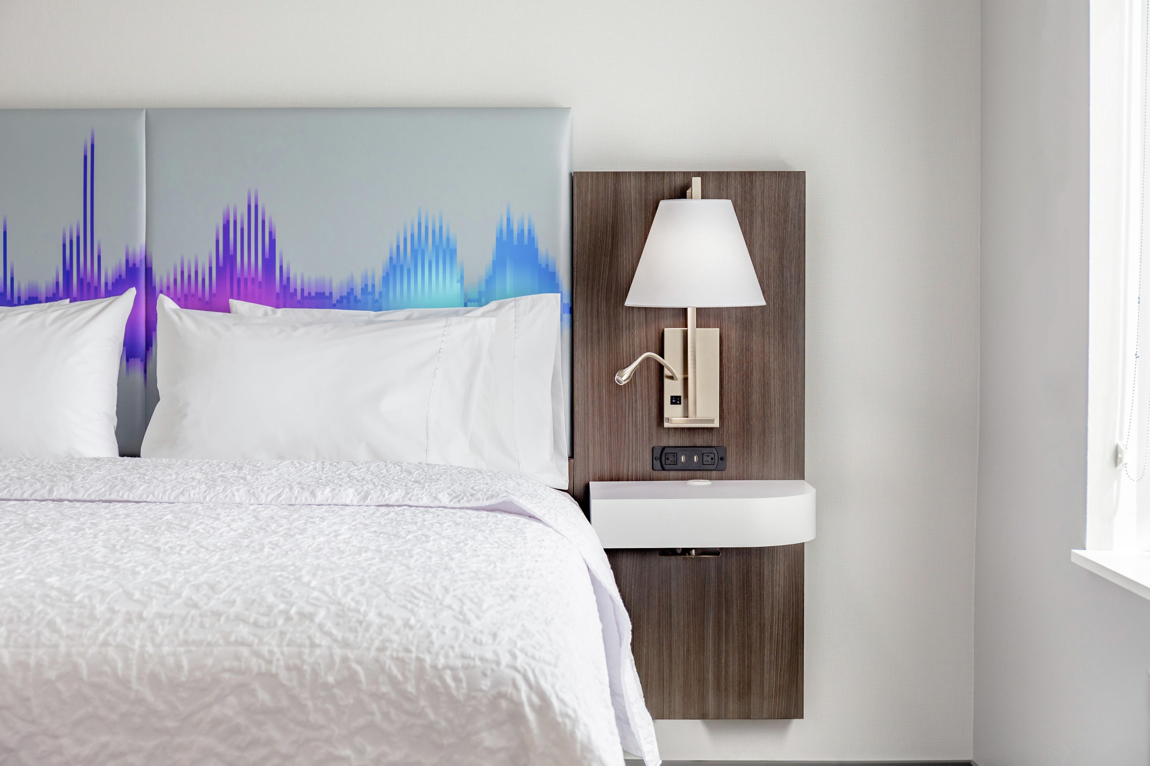 A hotel room with a bed, a wall-mounted lamp, and a sink.