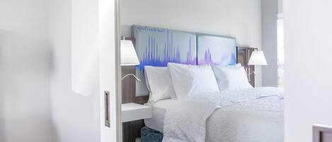 A hotel room with a bed, bedside lamps, a nightstand, and a wall-mounted artwork.
