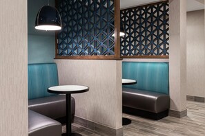 A seating area with two round tables and cushioned booths, featuring a geometric patterned partition and a wooden floor. - Hampton Inn & Suites Bridgeview Chicago (Summit)