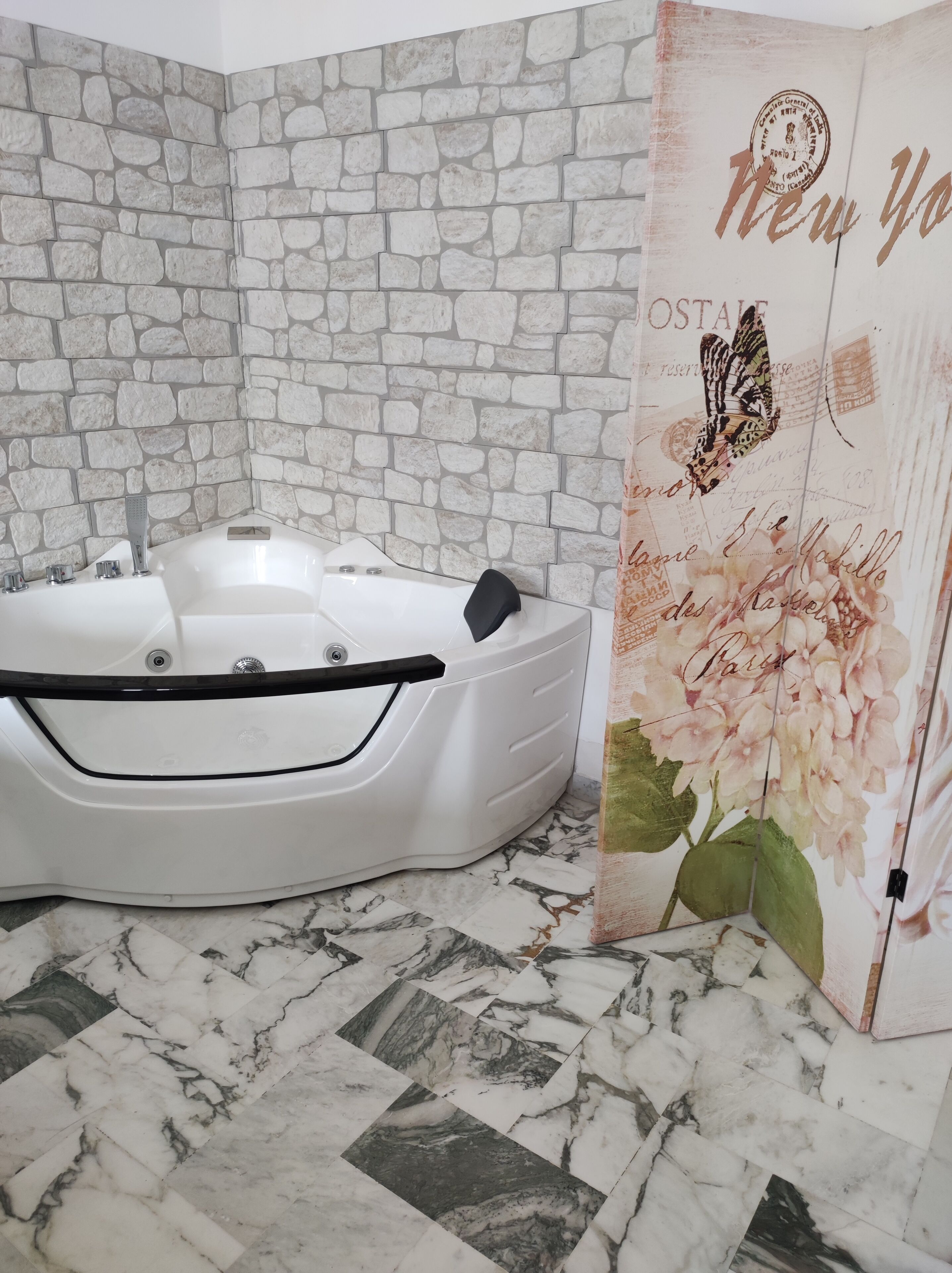 A bathroom with a white bathtub, a stone wall, and a door with a butterfly and flowers.