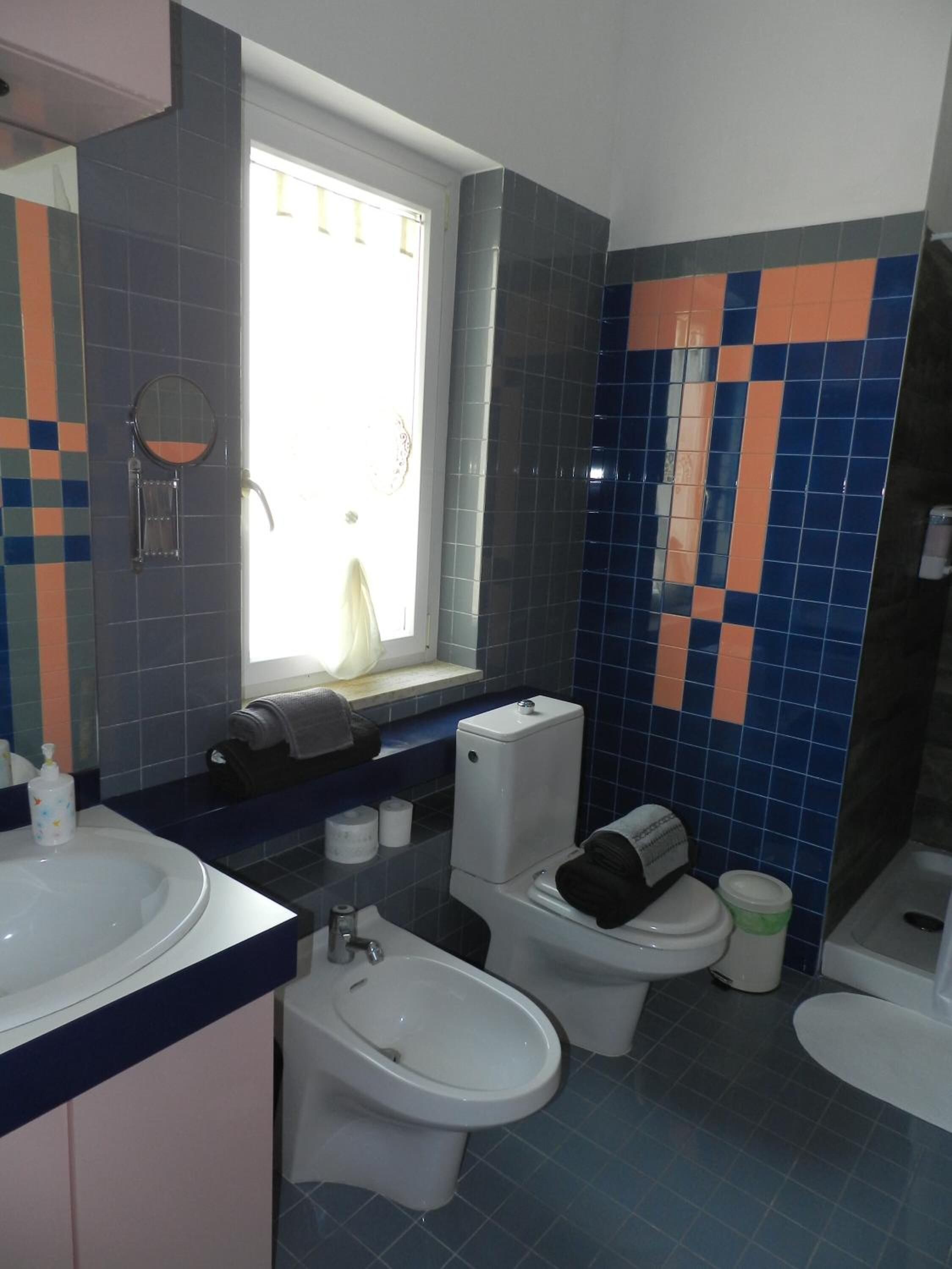 Een badkamer met een wastafel, twee toiletten, een bidet en een raam.