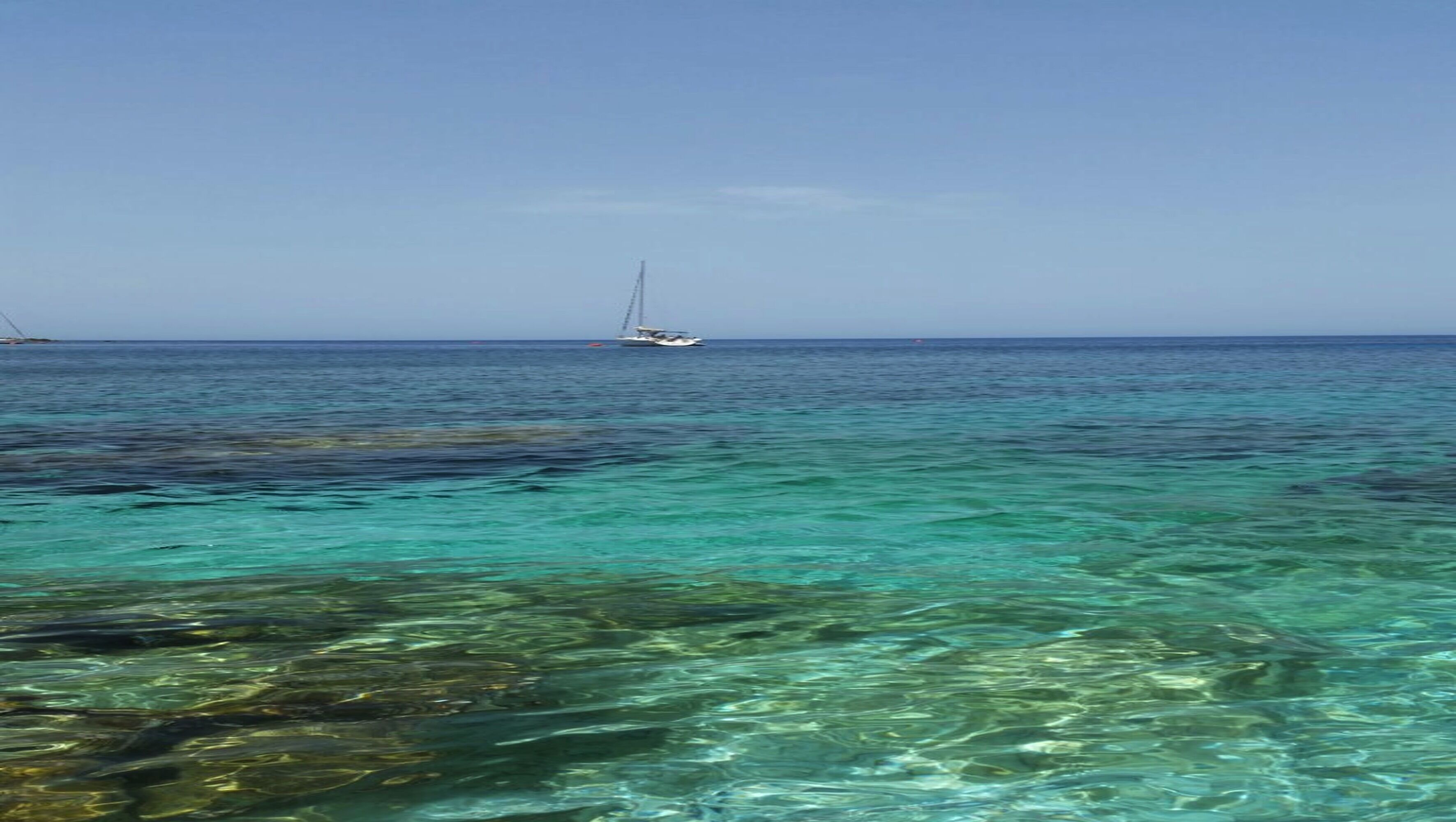 A clear view of turquoise waters with a sailboat in the distance.