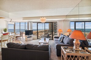 Ein geräumiges Wohnzimmer mit großem Fenster, einem Flachbildfernseher und einem Balkon mit Meerblick.