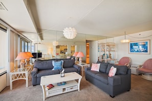 A modern living room with two sofas, a coffee table, and a TV. There are lamps, a mirror, and a painting on the walls. - XPLORIE ACTIVITIES & LINENS INCLUDED*! CAPRI 2BR/2BA condo with ocean and bay views! (Ocean City)