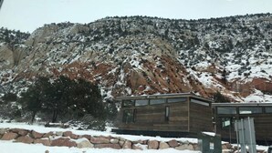 A cabin with a stone foundation, surrounded by snow-covered ground and a forested mountain. - Mini farmhouse style container Homes #3 (Orderville)