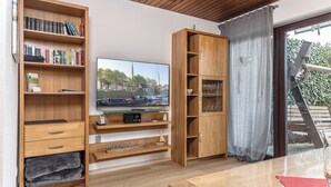 Ein modernes Wohnzimmer mit einer Holzbücherwand, einem Flachbildfernseher und einer Glastür zu einem Außenbereich.