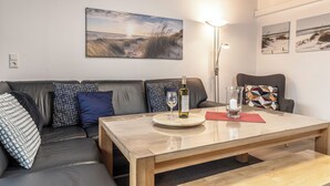 Ein modernes Wohnzimmer mit Holzboden, einer Couch mit gemusterten Kissen, einem Couchtisch mit einer Weinflasche und einem Glas sowie einer Wandlampe.