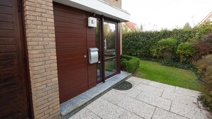 Ein modernes Gebäude mit Backsteinfassade, einer braunen Tür und einem kleinen Garten mit Hecke und Rasen.