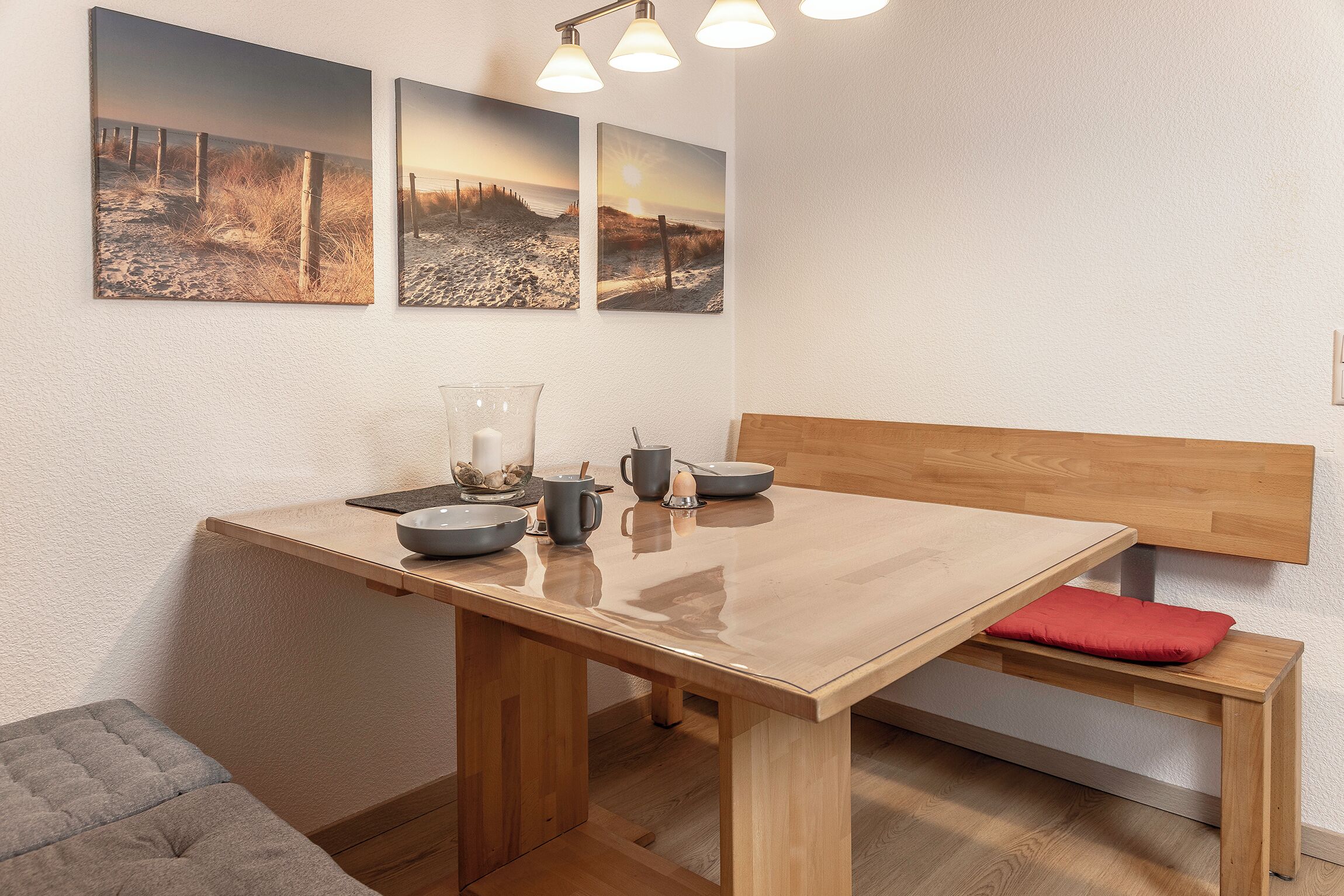 A dining area with a wooden table, bench, and three framed beach pictures on the wall.