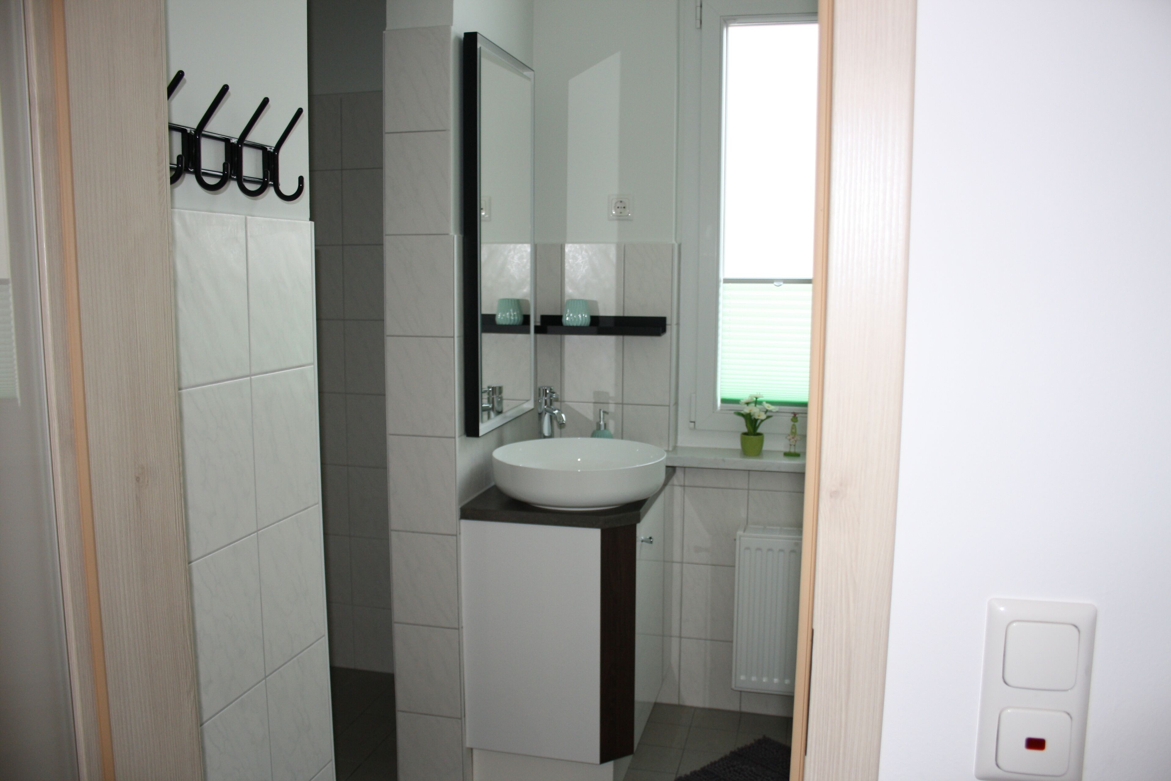 Une salle de bain moderne avec un lavabo blanc, des meubles sombres, un miroir et une fenêtre donnant sur un beau paysage.