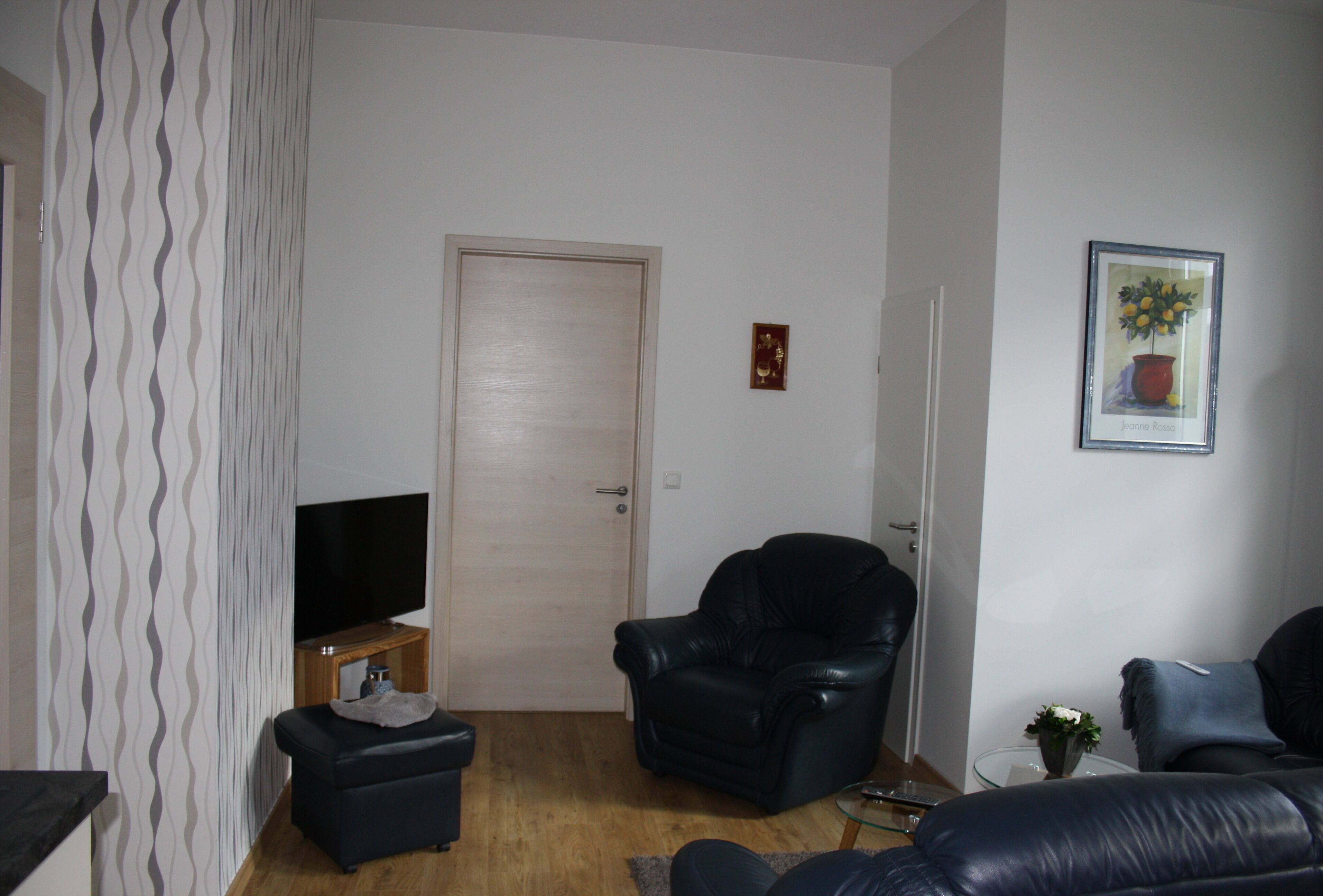 Un salon avec un téléviseur, un fauteuil en cuir noir, un canapé et une porte.