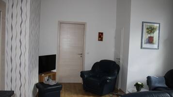 Un salon avec un téléviseur, un fauteuil en cuir noir, un canapé et une porte.