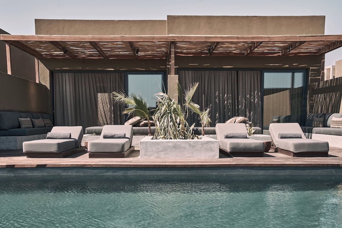 Un área de piscina moderna al aire libre con sillones reclinables, una zona de estar cubierta y un amplio ventanal.