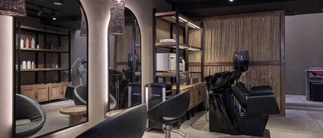 Un moderno salón de belleza con sillas negras, un espejo grande y estantes con productos para el cabello.