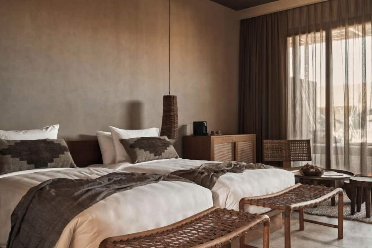 Un dormitorio con una cama grande, una lámpara colgante, una mesita de noche y vistas al exterior a través de cortinas traslúcidas.