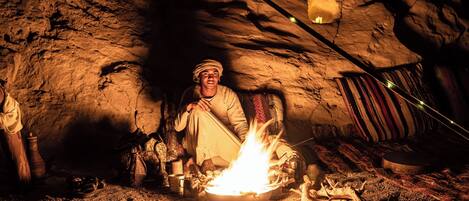 A cave interior with a fire, stone walls, and a striped fabric hanging.