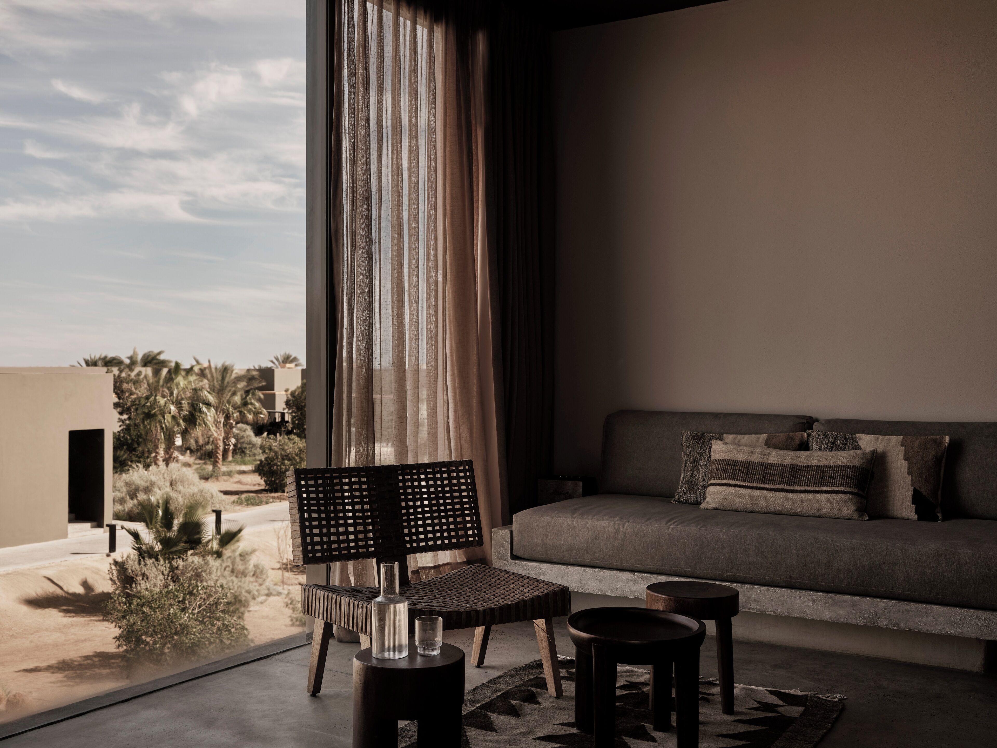 A modern living room with a sofa, two side tables, a chair, and a large window with curtains.