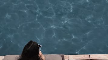 A person relaxing on a wooden deck by a clear pool with a small island.