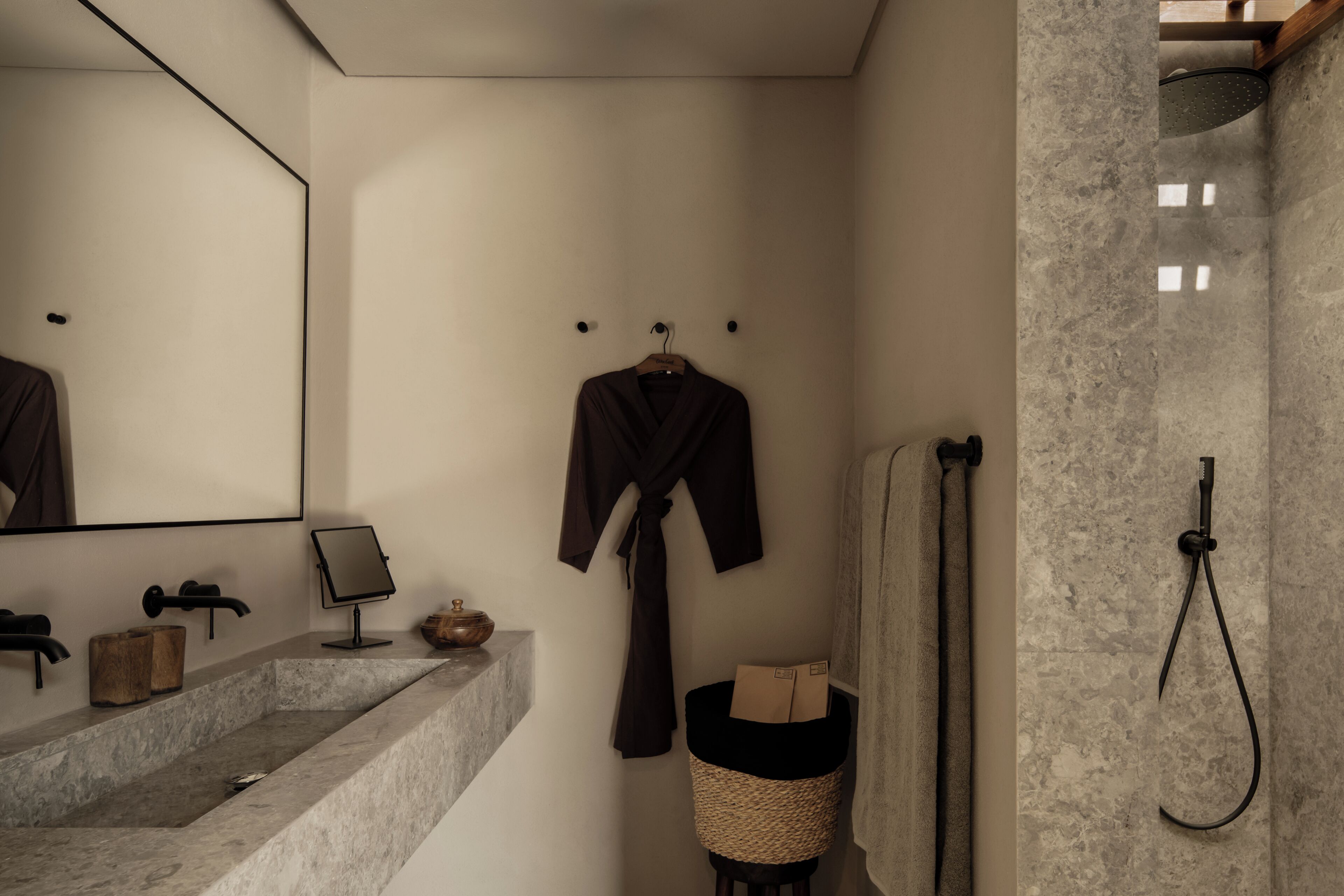 A bathroom with a marble sink, a mirror, a robe, a towel rack, and a shower.