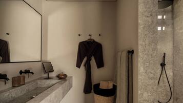 A bathroom with a marble sink, a mirror, a robe, a towel rack, and a shower.