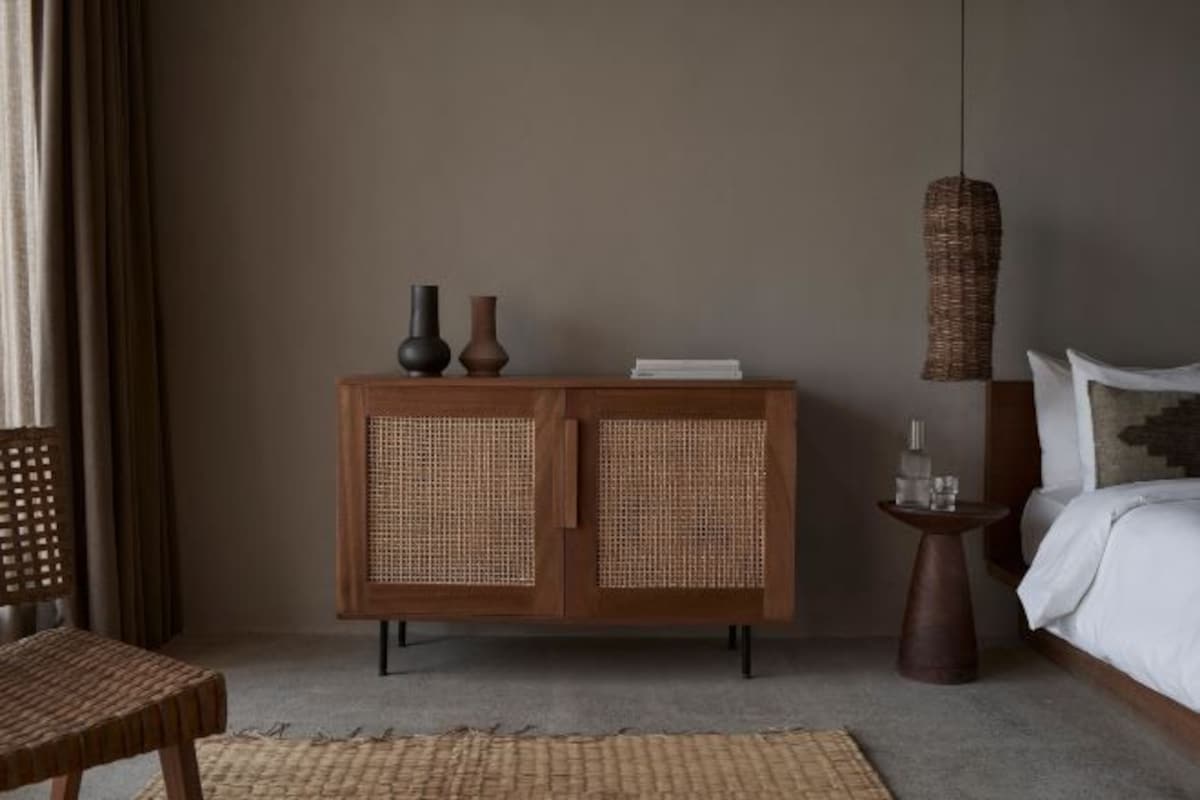 Une chambre à coucher comprenant un lit, une armoire en bois aux portes tressées, une petite table d’appoint et un luminaire suspendu tressé.
