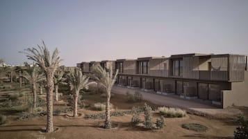 Un bâtiment moderne doté de nombreux balcons et de grandes fenêtres, entouré d’un jardin aménagé avec des palmiers et des arbustes.