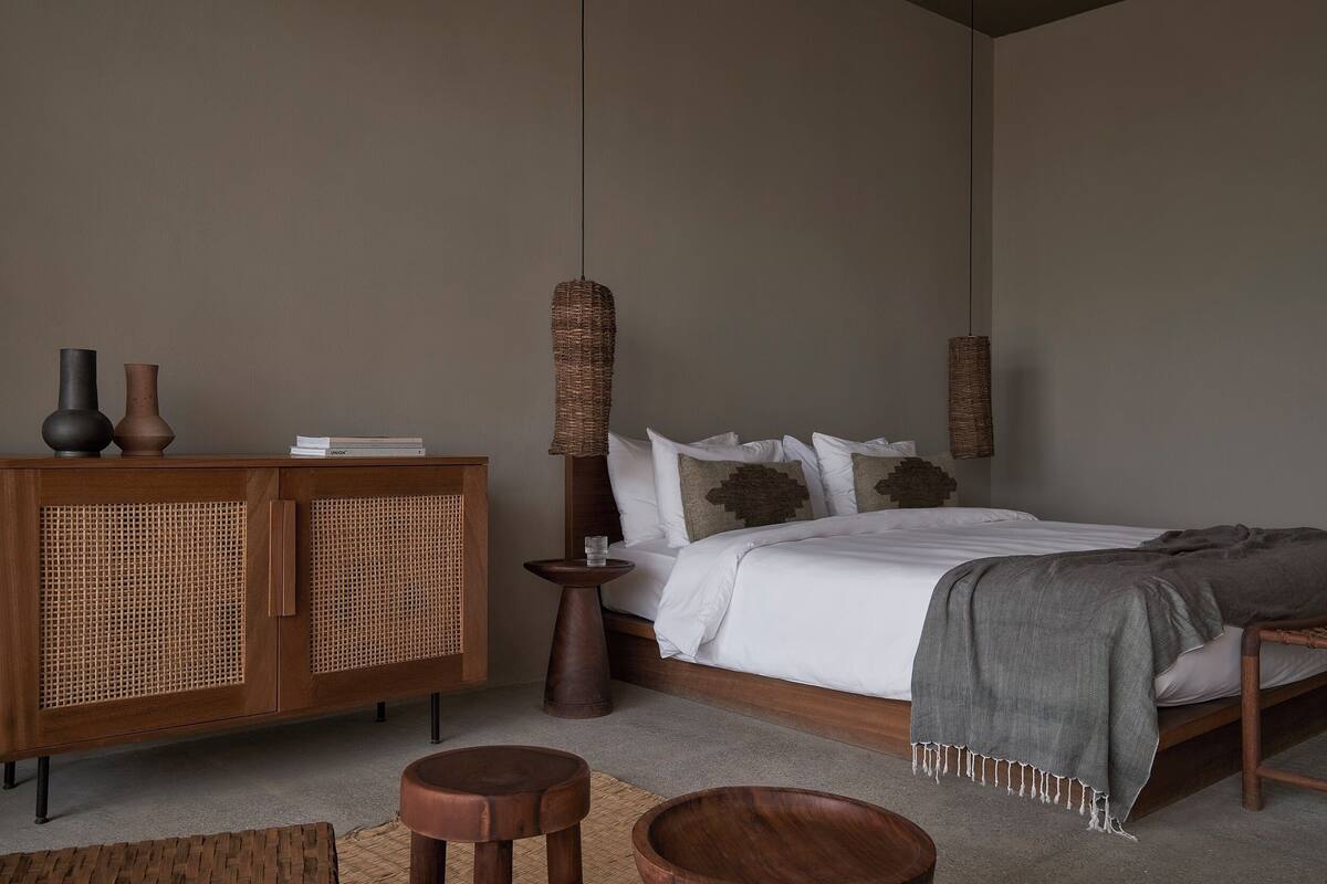 Un dormitorio con un armario de madera, una cama con ropa de cama blanca y dos lámparas colgantes.