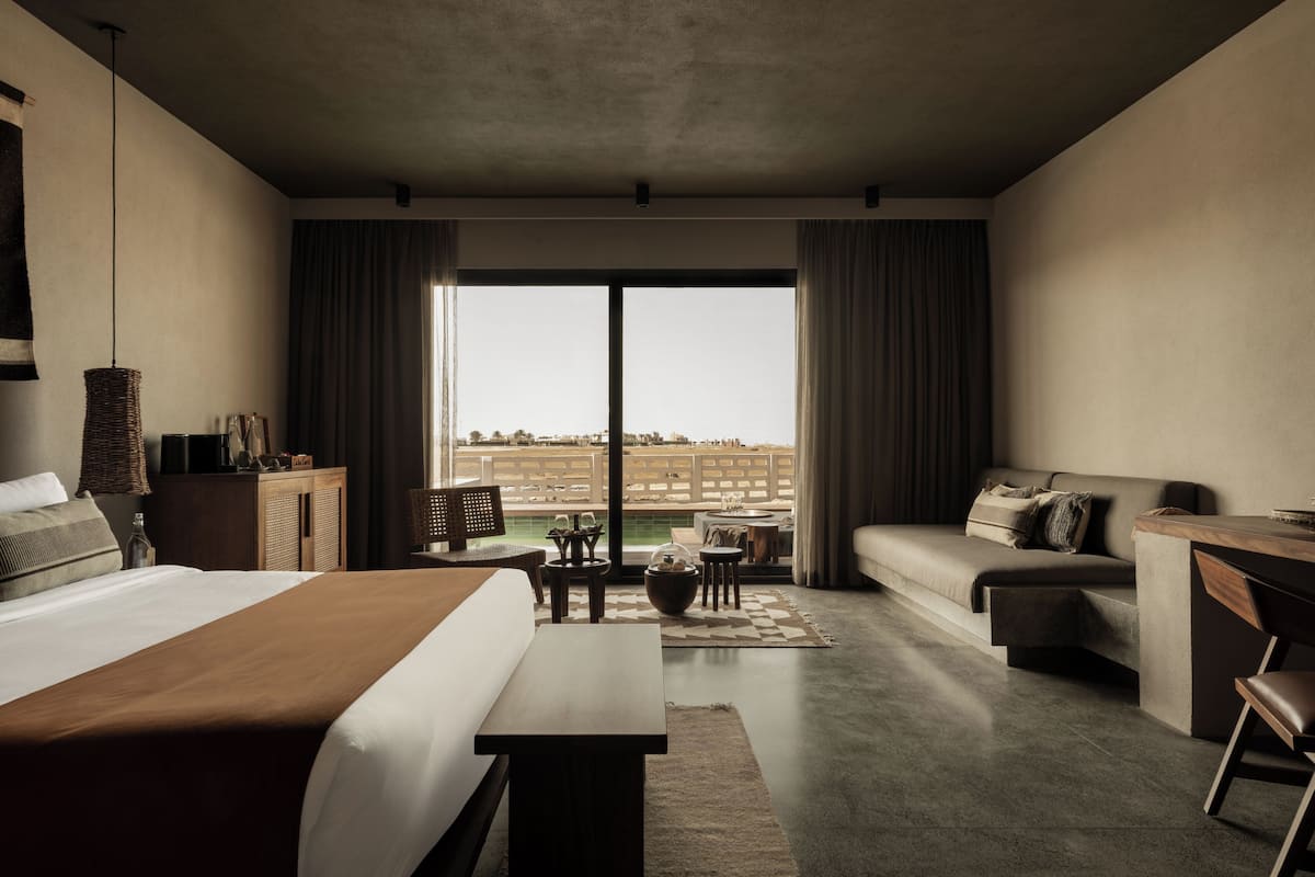 Una habitación de hotel moderna con una cama grande, un escritorio, un sofá y un balcón con vistas a la ciudad.