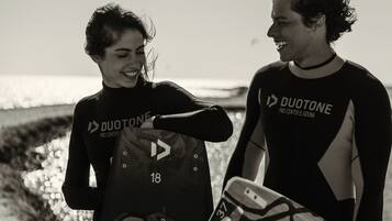 Two individuals in wetsuits holding surfboards on a beach.