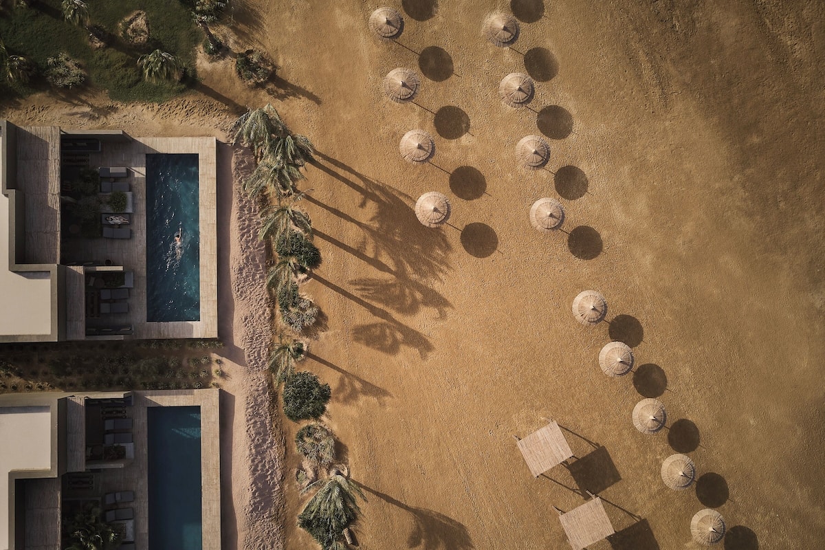 Vista aérea de un complejo turístico con piscina, mobiliario exterior y sombrillas.