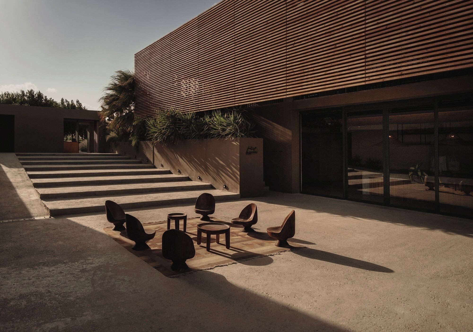 A modern building with a sloped roof, a staircase leading to a covered area, and outdoor seating with chairs and tables.
