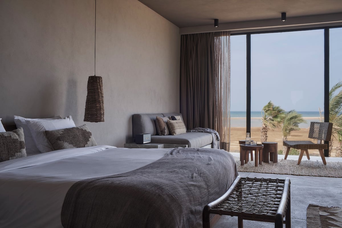 Una habitación de hotel moderna con una cama grande, un área de descanso con vista a la playa y un balcón con vista al océano.