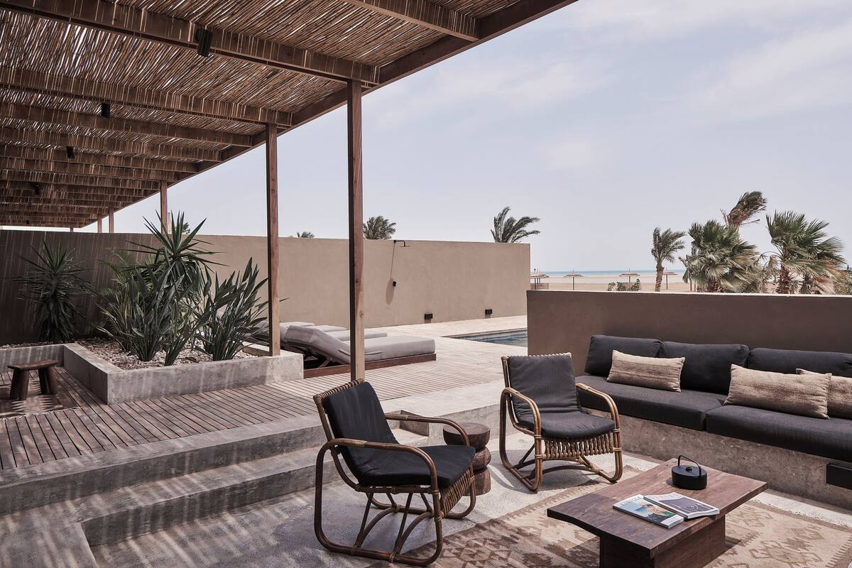 Una terraza en la azotea con mobiliario de mimbre, una piscina y palmeras.