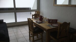 A dining area with a wooden table set for four, a window with a view of snow-covered ground, and a tiled floor.