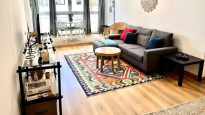 A living room with a grey sofa, a round wooden coffee table, a colorful rug, and a dining area with a white table and chairs. - Guia Acacias Apartment (Cascais)