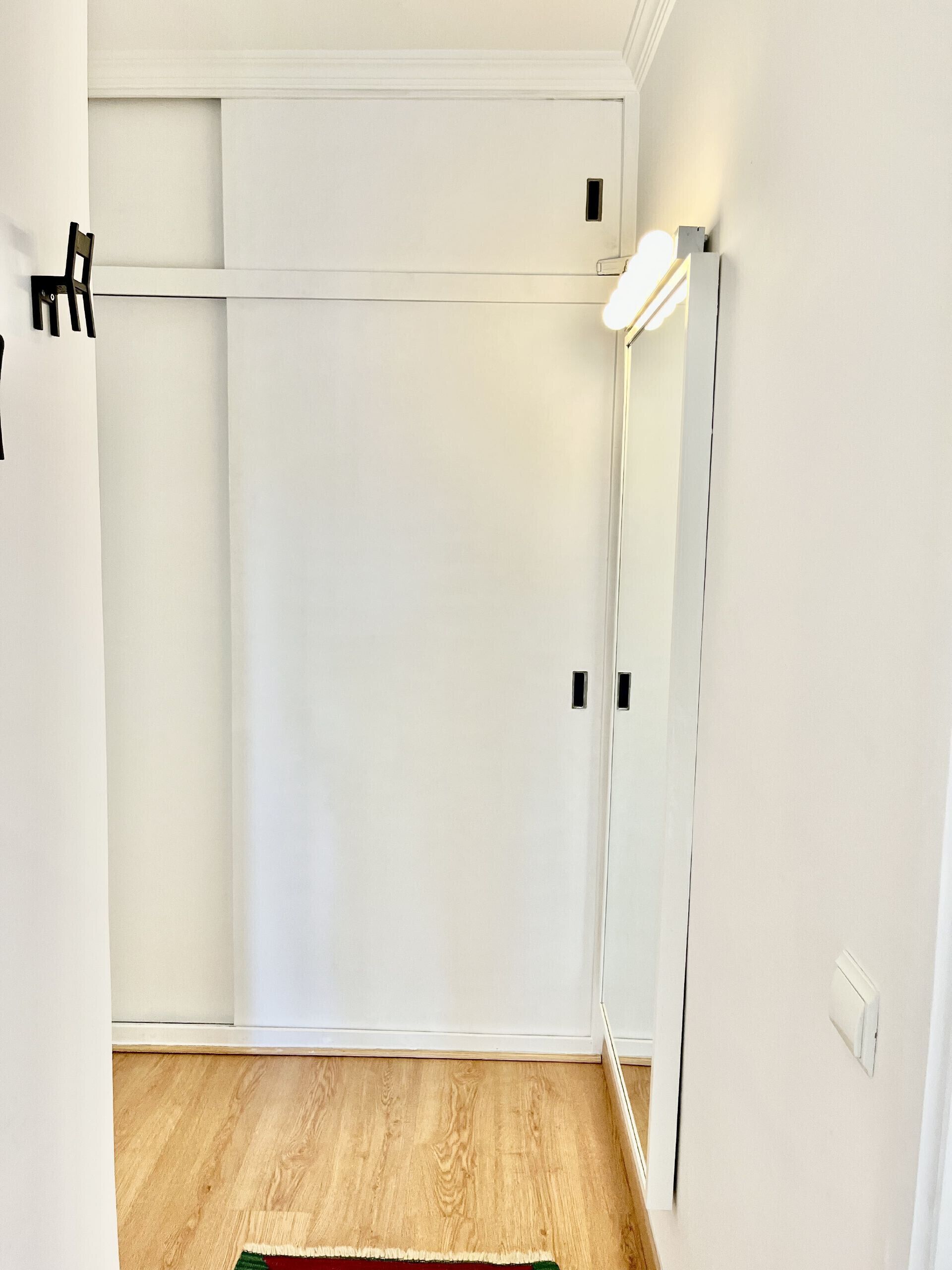 A room with a wooden floor, a white door, and a mirror reflecting part of the room.