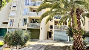 A multi-story residential building with balconies, a palm tree, and a paved driveway. - Guia Acacias Apartment (Cascais)