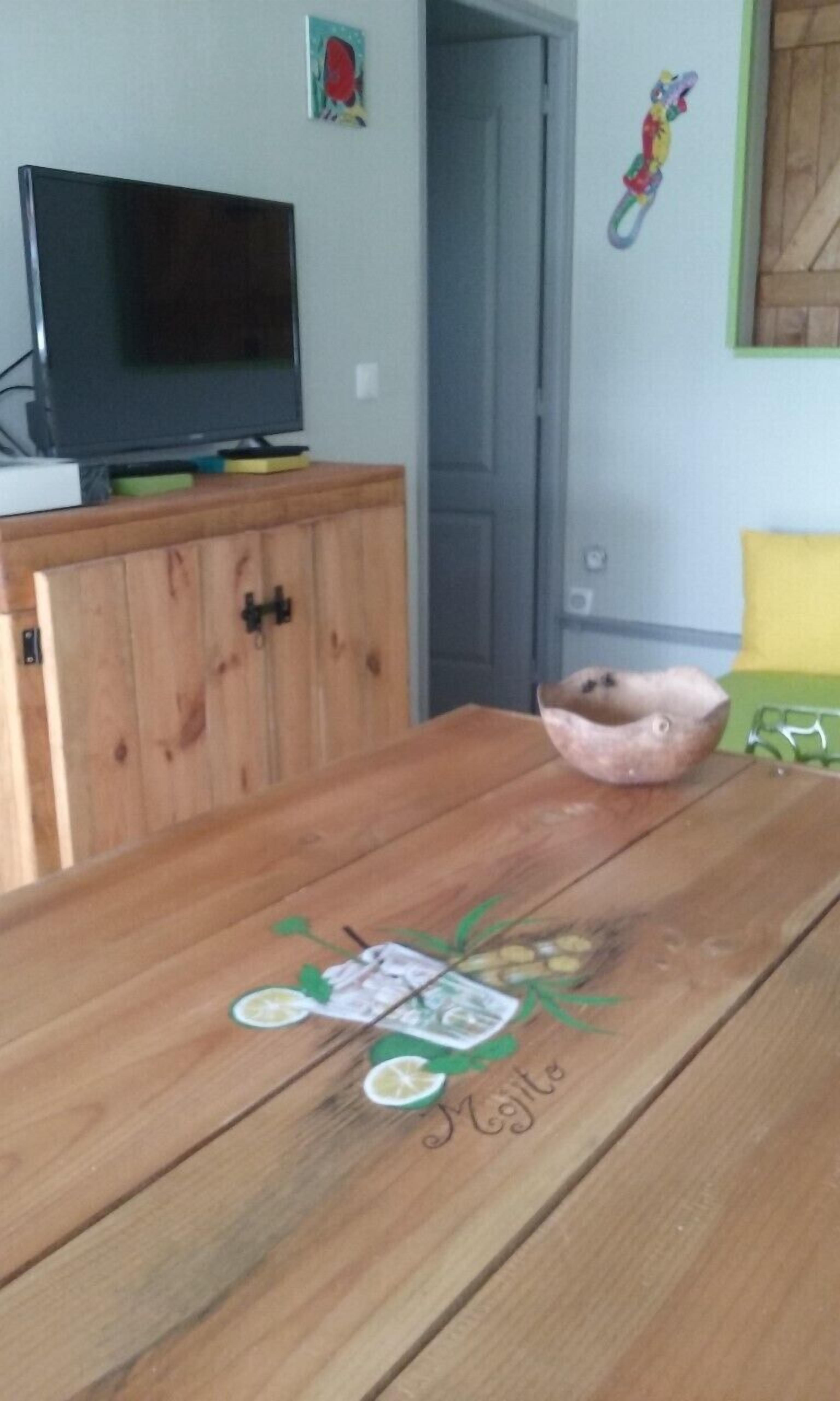 A wooden table with a painted design, a television on a wooden cabinet, and a door in the background.