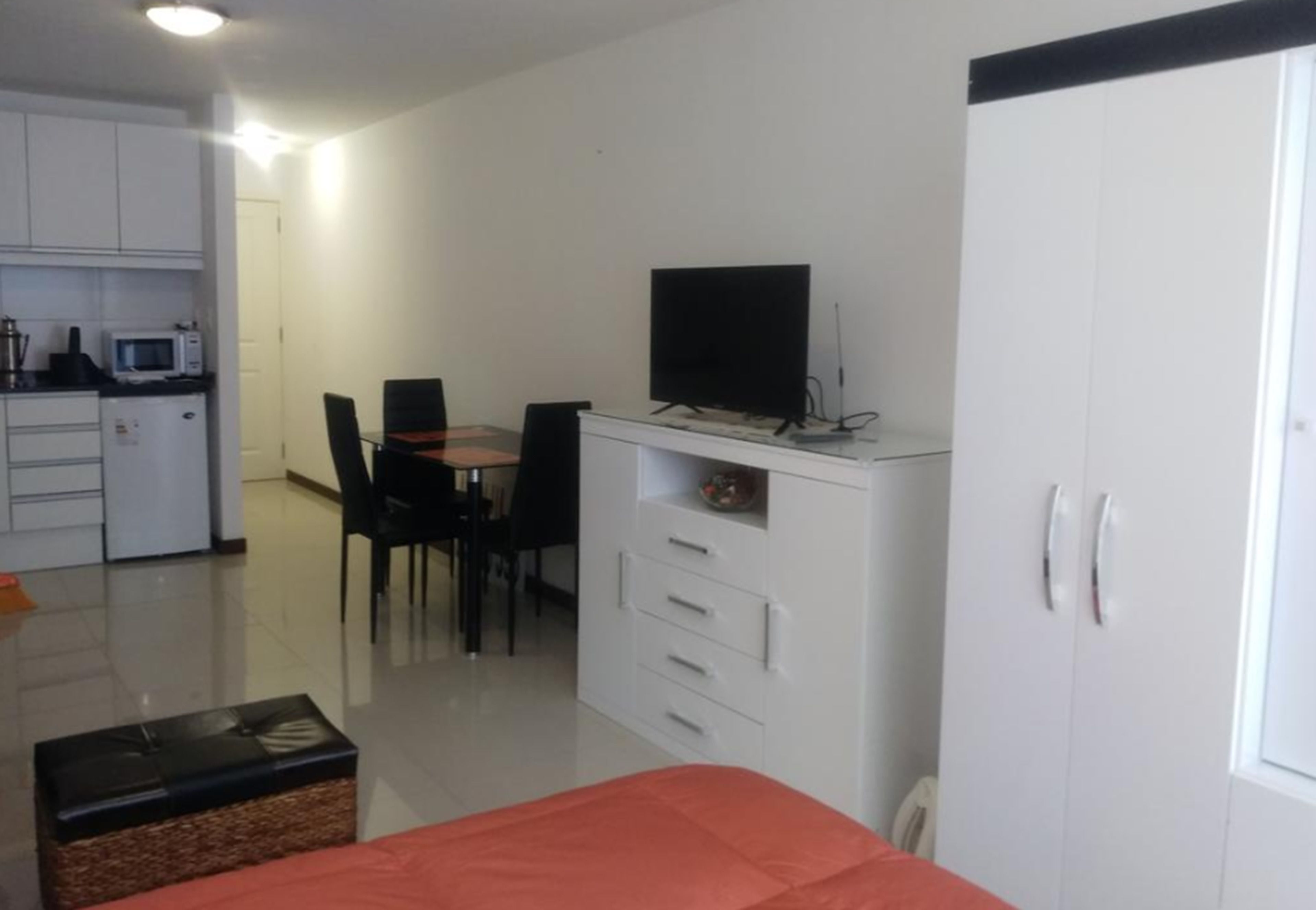 A compact room with a bed, a desk with a computer, a television, and a kitchenette.