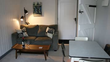 A cozy living room with a sofa, a coffee table with wine glasses, a painting on the wall, and a door with a handle.