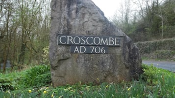 En stor sten med en skylt som visar texten ”CROSCOMBE AD 706”, omgiven av grönska och påskliljor.