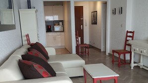 A modern living room with a white sofa, red chairs, and a dining table. A kitchen is visible in the background. - Apartment 2 Rooms + Terrace 10 m² -Front de Mer, Face Plage de Sable  (Bandol)