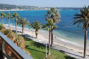 A coastal view with palm trees, a beach, and a clear blue sea.