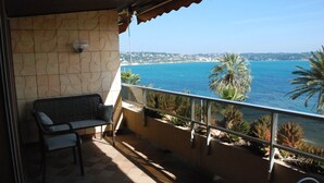 A balcony with a stone wall, a cushioned bench, and a view of the sea and distant buildings. - Apartment 2 Rooms + Terrace 10 m² -Front de Mer, Face Plage de Sable  (Bandol)