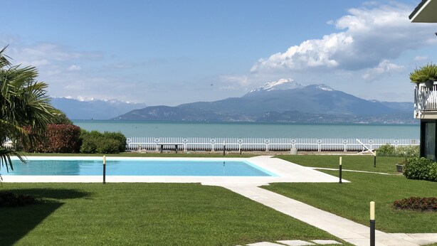 A swimming pool with a view of a lake and mountains in the background. - Lakefront apartment with pool and WiFi (Sirmione)