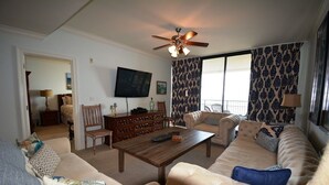 A living room with a sofa set, a wooden coffee table, a television, and a ceiling fan. - Best seat in the house! FALL RATES, NO CROWDS, RENT A GOLF CART, WALK THE BEACH. (Dauphin Island)