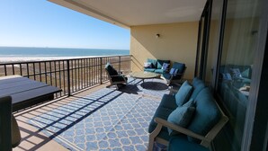 A balcony with a view of the beach, a sofa, a table, and a patterned rug. - Best seat in the house! FALL RATES, NO CROWDS, RENT A GOLF CART, WALK THE BEACH. (Dauphin Island)
