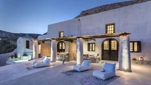 A modern outdoor seating area with white lounge chairs and a pool, surrounded by a white building with large windows and columns. - Canava Villas #2 with Private Pool @Medieval Village , Santorini (Santorini)