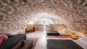 A cozy, stone-walled room with a bed, a sofa, and a small seating area. - Canava Villas #2 with Private Pool @Medieval Village , Santorini (Santorini)